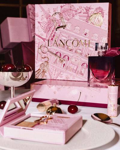 Unnepi Lancome holiday display nagy illusztralt rozsaszin ajandekdobozzal, parfummel es sminktermekekkel egy asztalon, friss cseresznyekkel elrendezve.