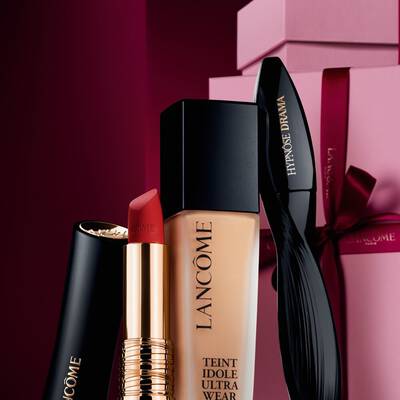 Elegans csendelet a Lancome L'Absolu Rouge matt ruzsaval, a Teint Idole Ultra Wear alapozoval es a Hypnose Drama szempillaspirallal, fenyuző sotetvoros unnepi hatter előtt.