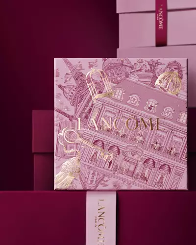 Kep egy rozsaszin Lancome unnepi ajandekdobozrol, amely rozsaszin es sotetvoros ajandekdobozok halma előtt all, sotetvoros hatter előtt.