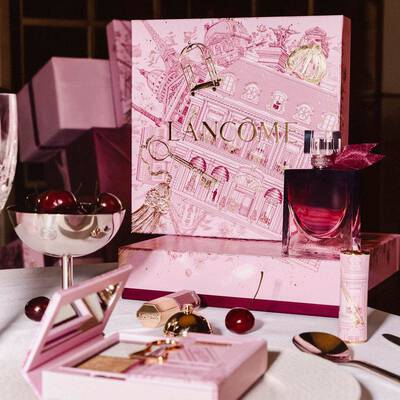 Unnepi Lancome holiday kollekcios display egy asztalon, nagy illusztralt rozsaszin ajandekdobozzal, parfummel, sminktermekekkel es friss cseresznyekkel.