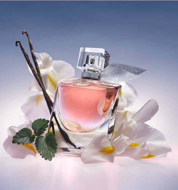 Rozsaszin parfum uveg viragok es vaniliarud mellett, lagy fenyben.