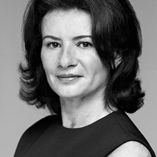 A black and white portrait of a woman with shoulder-length dark hair, wearing a sleeveless dress and looking confidently at the camera.