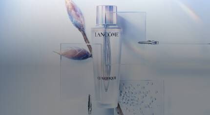 A kepen egy Lancome Clarifique nevu bőrapolo termek lathato uvegcse formajaban, amely mellett vizcseppek es novenyi motivumok talalhatok.