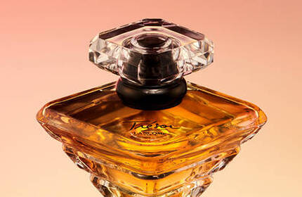 A close-up of an elegant perfume bottle with a diamond-shaped cap, filled with golden liquid, set against a soft gradient background.