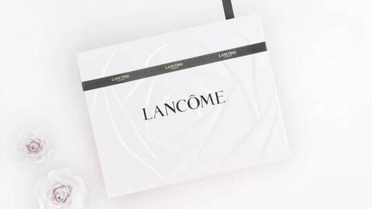 Feher Lancome ajandekdoboz, rozsakkal diszitve, elegans szurke szalaggal atkotve.