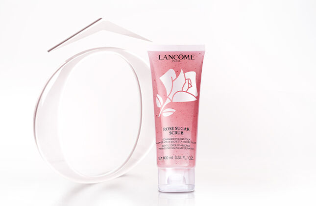 A tube of skincare product next to a circular mirror, both displayed against a soft, light background. The product has a pink and white design.