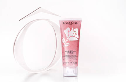 A tube of skincare product next to a circular mirror, both displayed against a soft, light background. The product has a pink and white design.