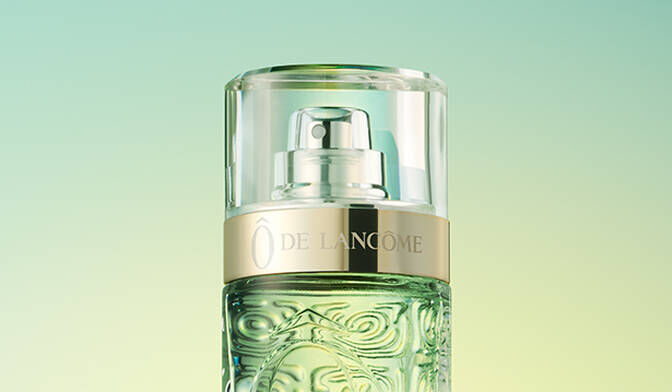 A close-up of a perfume bottle with a gold cap against a soft gradient background in green tones.