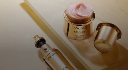 Ket Lancome kozmetikai termek: egy arckrem es egy szerum, elegans arany csomagolasban, leheletnyi fenyben.