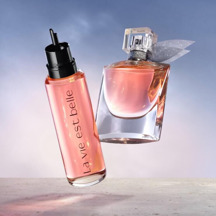 Ket parfum lebeg egy vilagos hatter előtt, az egyik uveg fekete kupakkal es "la vie est belle" felirattal, a masik uveg atlatszo, masnival diszitve.