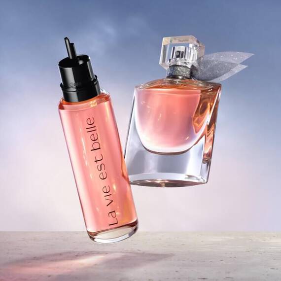Ket parfum lebeg egy vilagos hatter előtt, az egyik uveg fekete kupakkal es "la vie est belle" felirattal, a masik uveg atlatszo, masnival diszitve.