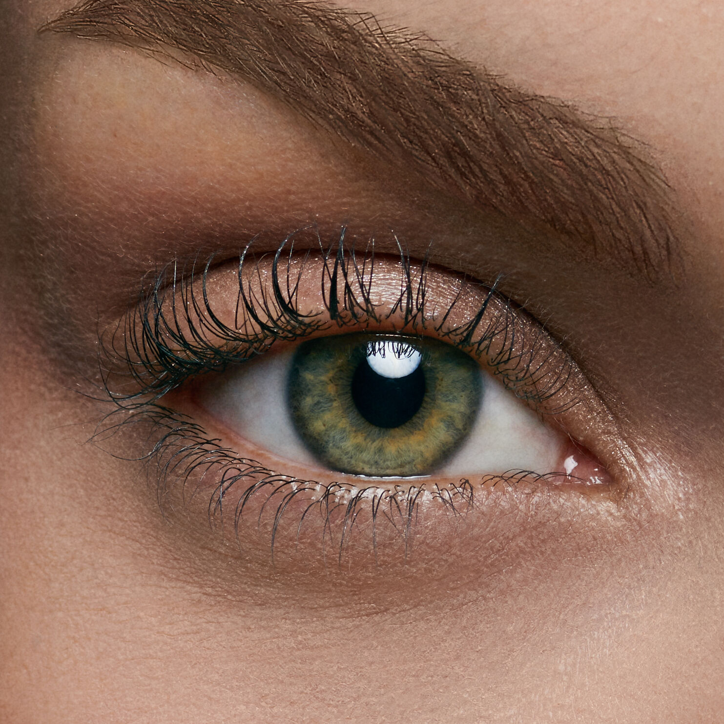 Close-up of a human eye with green and brown hues, featuring long eyelashes and a well-defined eyebrow.