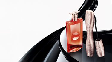 A collection of elegant pink cosmetic products, including a perfume bottle and a mascara, arranged against a soft, neutral background.