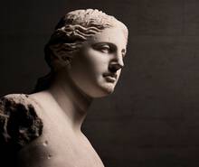 A close-up view of a classical marble bust of a woman, highlighting her profile and detailed facial features, with soft lighting emphasizing the texture of the stone.