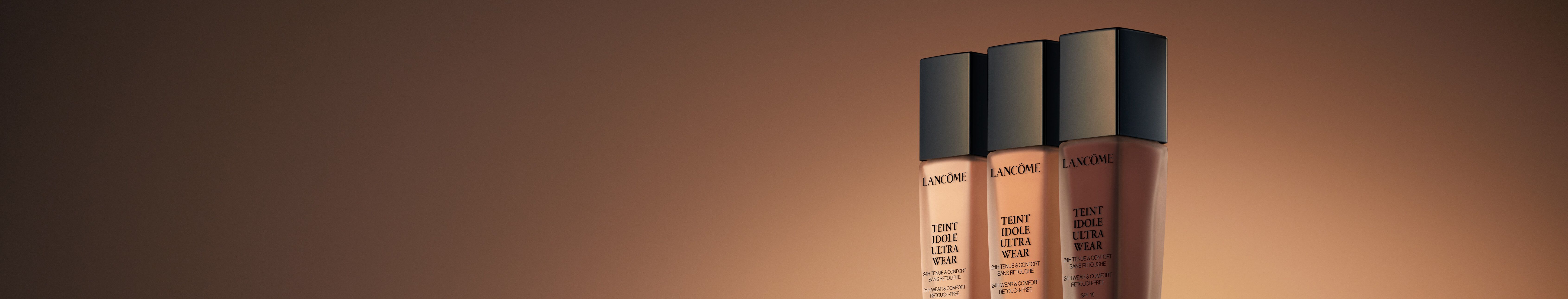 Three bottles of Lancome foundation in various shades, elegantly displayed against a warm, gradient background.