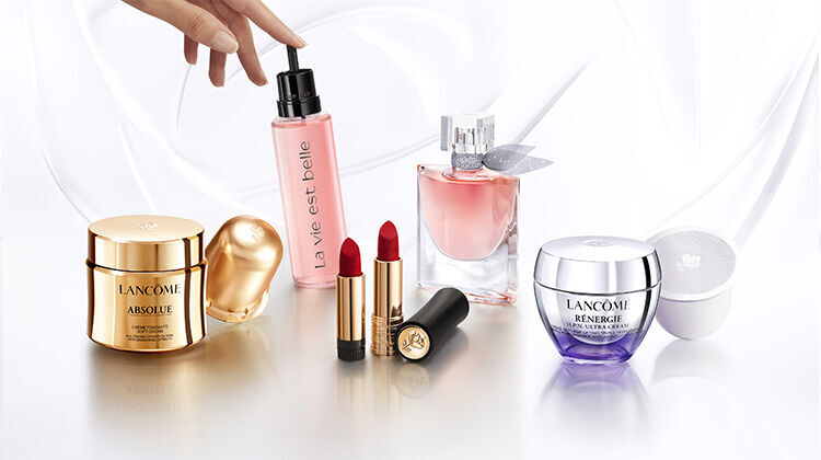 A display of various beauty products, including a moisturizer, a pink spray, a perfume, lipstick, and a cream, arranged elegantly on a light background.