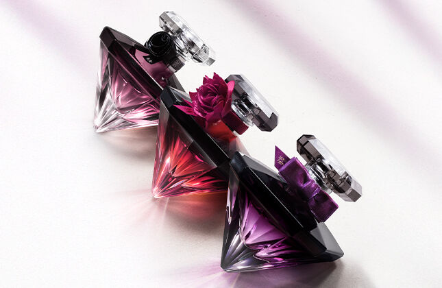 Three elegantly designed perfume bottles in shades of pink and purple are arranged on a light surface, casting soft shadows.