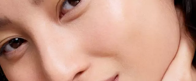 Close-up of a person's face, focusing on their skin and eyes, with a softly lit background.