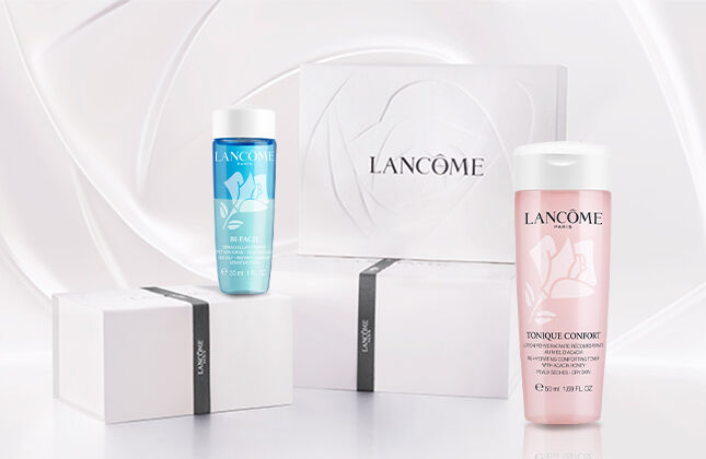 A collection of Lancome skincare products displayed on a soft, wave-like background. The products include two bottles, one blue and one pink, alongside a white box with the Lancome logo.