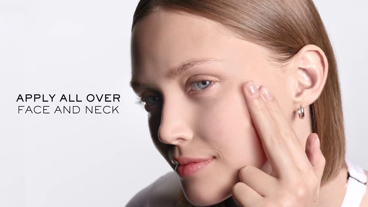 Fiatal nő, aki az arcát és nyakát krémmel kezeli, természetes sminkkel és nyugodt arckifejezéssel.