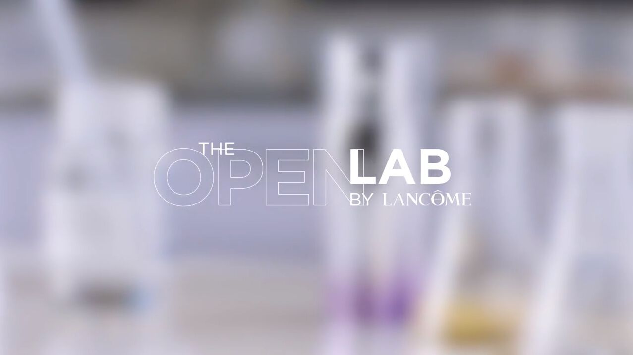 A kép a Lancôme 'The Open Lab' laboratóriumának feliratát mutatja, háttérben különböző szérumokkal.